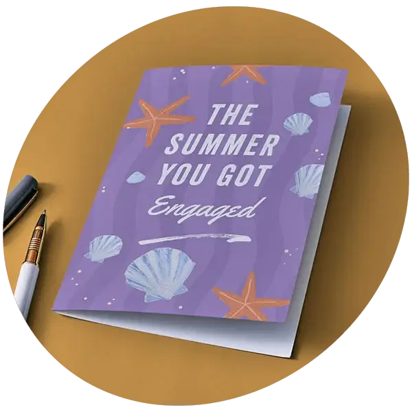 A purple engagement card decorated with seashells and starfish, displayed on a mustard-colored surface beside two pens.