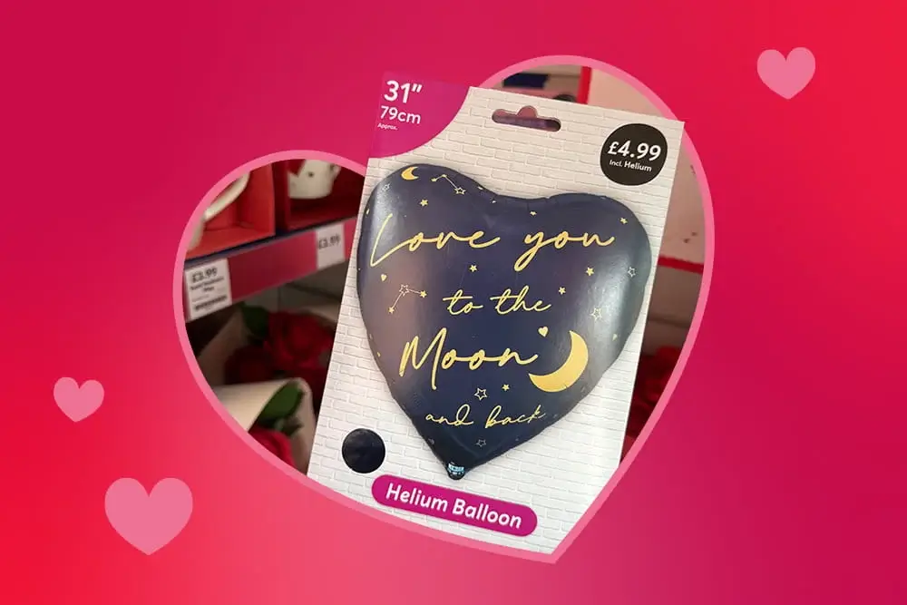 Heart‑shaped helium balloon package with a navy design that reads Love you to the Moon and back, displayed against a pink background with faint hearts.
