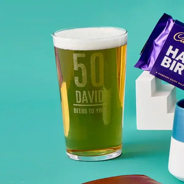 Pint glass filled with beer, personalised with a 50th birthday name and message, on a teal background