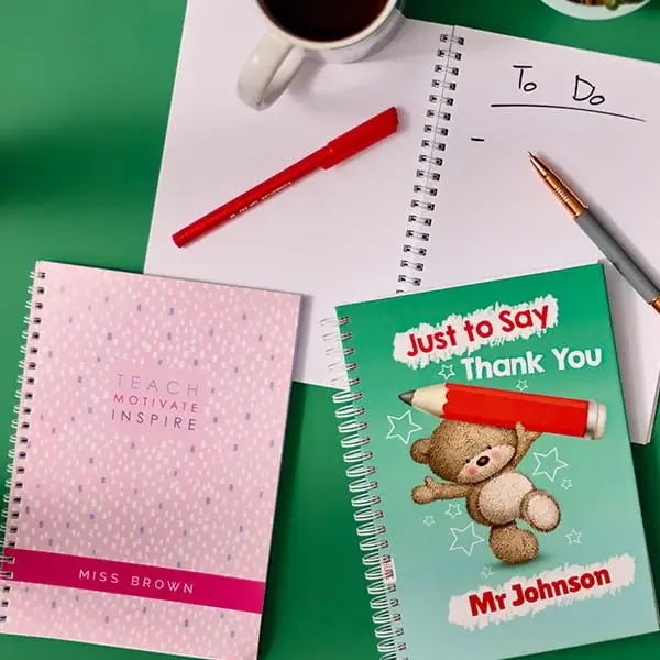 Notebooks and stationery including personalised teacher gift books, pens, and a to do list arranged on a green background