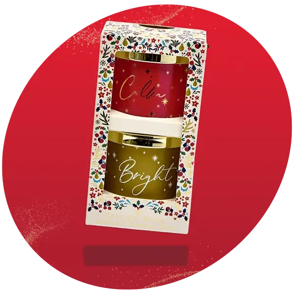 Gift set with two candles in a floral box, one red labeled Calm and one gold labeled Bright, displayed on a solid red background Gift set with two candles in a floral box, one red labeled Calm and one gold labeled Bright, displayed on a solid red background