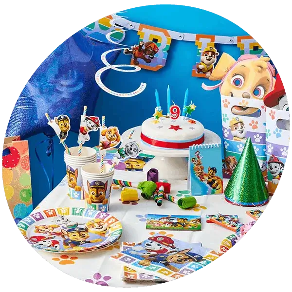 A colorful Paw Patrol-themed birthday party setup featuring a decorated cake with a number 9 candle, plates, cups, and napkins adorned with Paw Patrol characters. The table also includes party hats, gift bags, and various decorations such as a banner and hanging spirals.