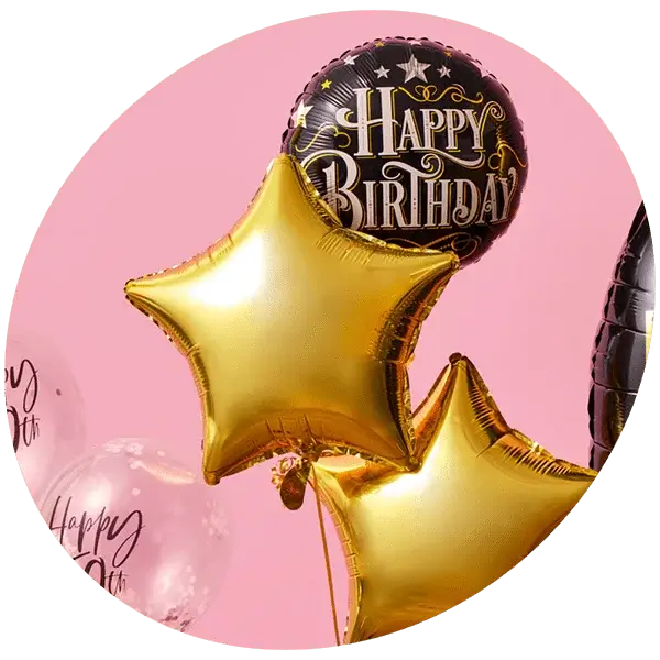 Cluster of birthday balloons including gold stars, a black Happy Birthday balloon, and a transparent balloon against a pink background.