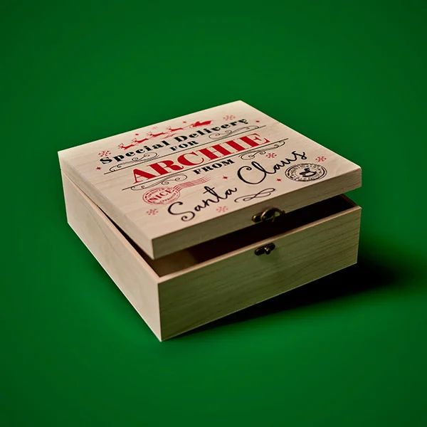 A wooden Christmas Eve box with an engraved lid reading ‘Special Delivery from the North Pole’ and ‘Christmas Eve Crate from Santa Claus,’ displayed slightly open against a green background.