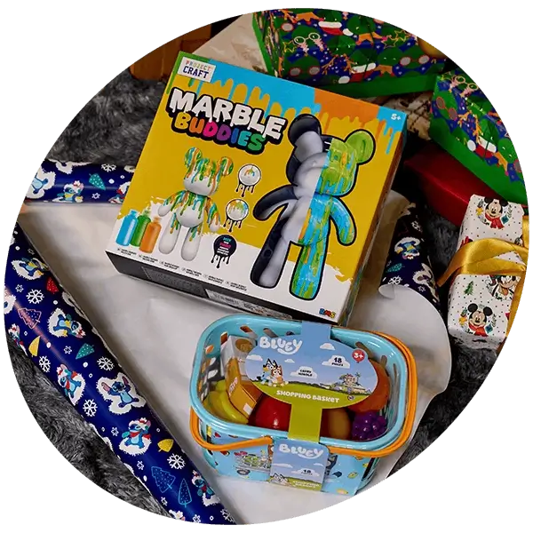 Marble Buddies craft kit and Bluey shopping basket toy displayed among wrapped Christmas presents and festive gift wrap.