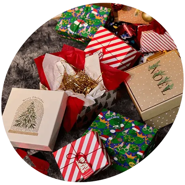 Wrapped Christmas presents and gift boxes in festive paper, ribbons, and gift bags arranged on a soft grey rug.