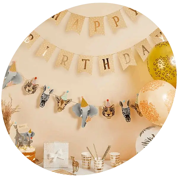 A jungle-themed birthday party display with a Happy Birthday banner, animal face garland, gold and patterned balloons, party cups, and decorations arranged on a table.