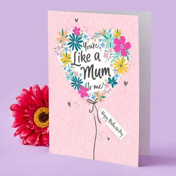 A pink Mother’s Day card featuring a heart-shaped floral design with bright, colourful flowers, displayed upright beside a vibrant pink flower.