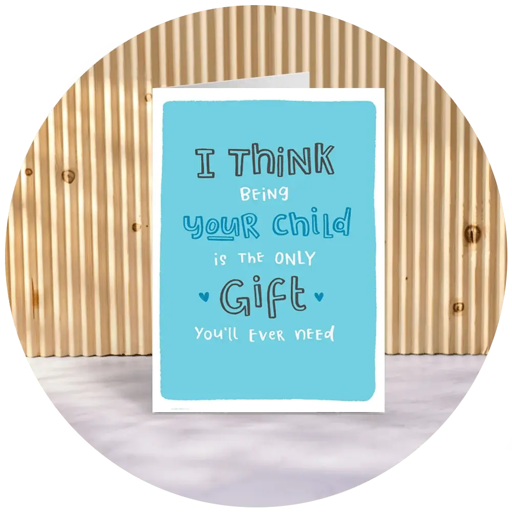 A greeting card with a blue front cover that reads, 'I THINK being your child is the ONLY Gift you'll ever need' in various fonts and sizes. The card is standing on a light-colored surface with a wooden background. A greeting card with a blue front cover that reads, 'I THINK being your child is the ONLY Gift you'll ever need' in various fonts and sizes. The card is standing on a light-colored surface with a wooden background.