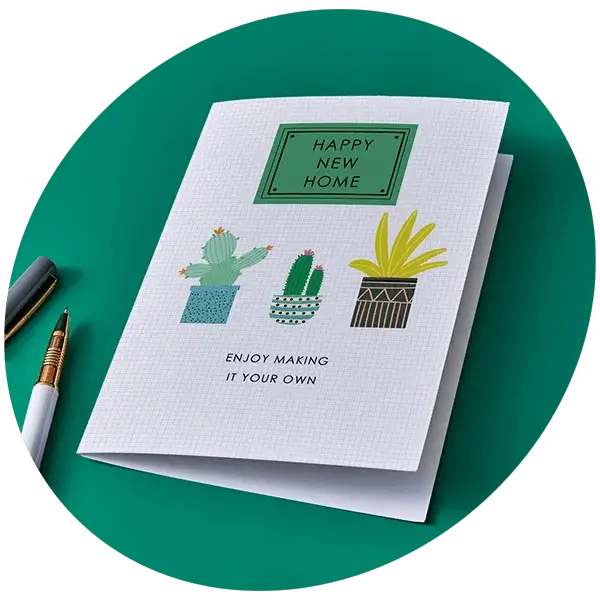 New home greeting card featuring illustrated houseplants and a welcoming message, displayed against a teal background with a pen nearby.