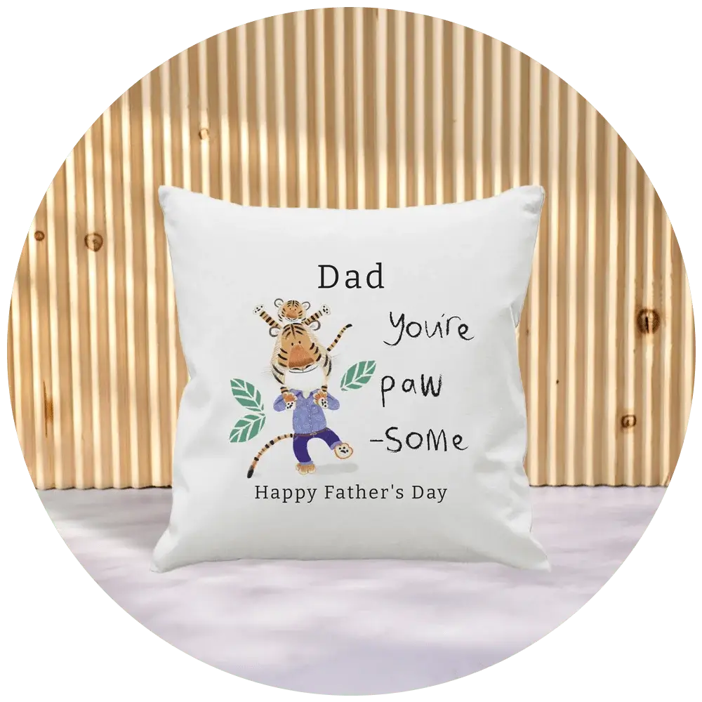 A white cushion with a design featuring a tiger holding a cub. The text on the cushion reads: Dad, you're paw-some. Happy Father's Day.' A white cushion with a design featuring a tiger holding a cub. The text on the cushion reads: Dad, you're paw-some. Happy Father's Day.'
