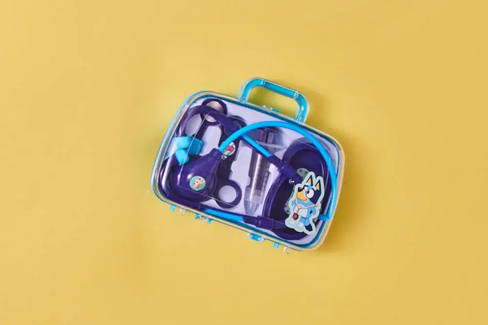 Clear plastic Bluey-themed medical kit with toy instruments, shown against a yellow background. Clear plastic Bluey-themed medical kit with toy instruments, shown against a yellow background.