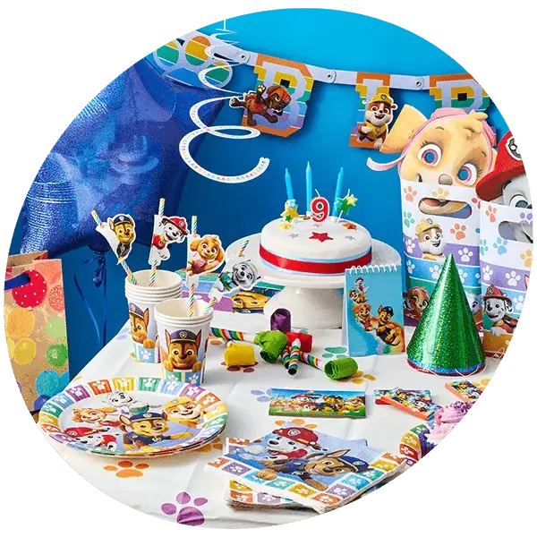 A colorful Paw Patrol-themed birthday party setup featuring a decorated cake with a number 9 candle, plates, cups, and napkins adorned with Paw Patrol characters. The table also includes party hats, gift bags, and various decorations such as a banner and hanging spirals.