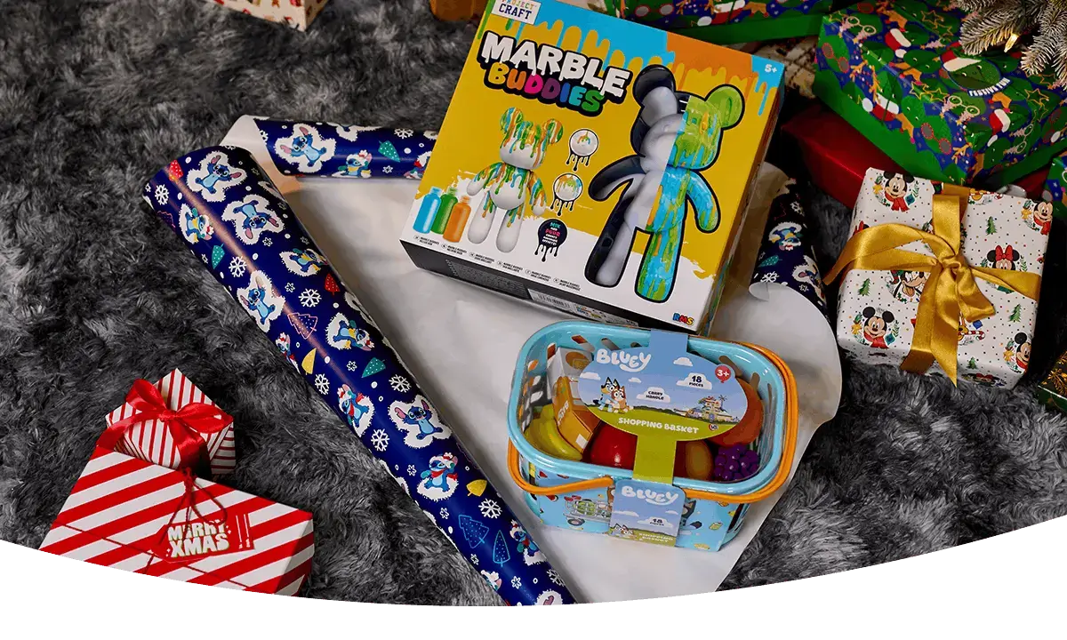 Bluey shopping basket toy and Colour Buddies craft set displayed among wrapped Christmas presents and festive gift wrap on a grey rug.