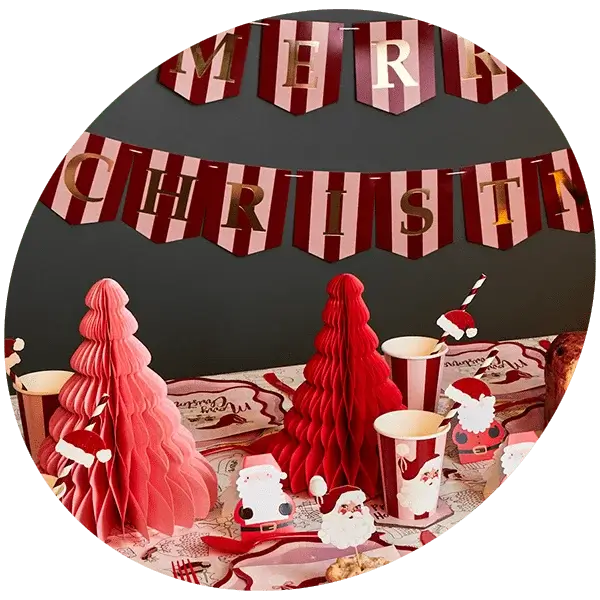 Christmas party table with red and pink paper trees, Santa-themed cups and decorations, and a red-striped Merry Christmas banner on the wall.