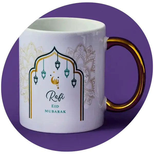 White ceramic mug with a gold handle, decorated with an arch design, hanging lanterns, and intricate patterns, featuring Eid Mubarak text on a purple background.
