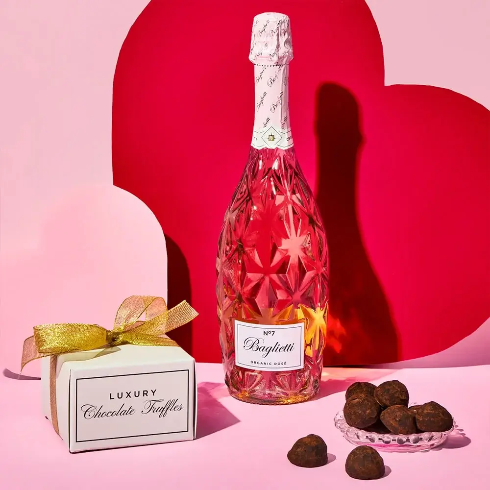 Nestlé Dairy Box The Classic Collection chocolate box with a pink and gold splash design on the lid, surrounded by assorted chocolates in various shapes, displayed on a pink background with a heart-shaped platform.