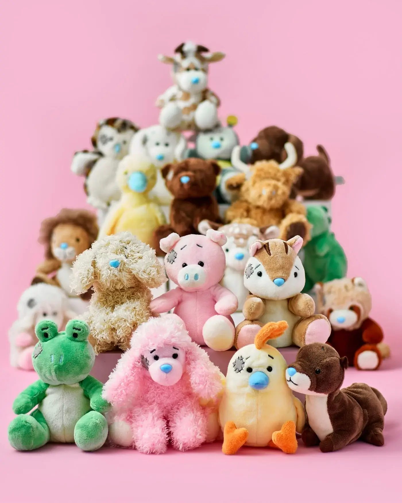 A group of various stuffed animals arranged in a pyramid formation against a pink background. The collection includes different animals such as a frog, poodle, pig, fox, duck, and others. Each plush toy has distinct features and colors.