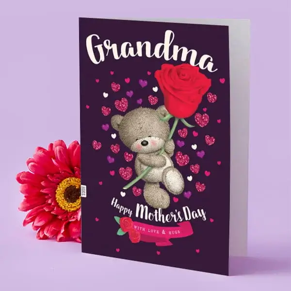 Mother’s Day card for a grandma featuring a cute teddy bear holding a large red rose, surrounded by pink and purple hearts, with a pink flower placed beside the card.