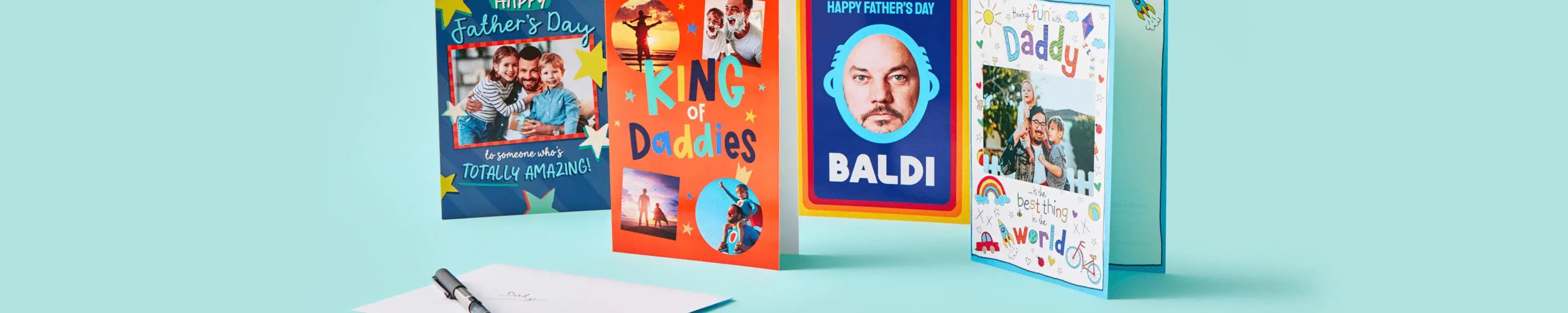 A row of colorful Father's Day cards is displayed against a light blue background. The cards feature various designs, including one with a photo of a father and child, another with the text 'King of Daddies,' and another with the word 'BALDI.' There is also an open card on a table in front of the row.' A row of colorful Father's Day cards is displayed against a light blue background. The cards feature various designs, including one with a photo of a father and child, another with the text 'King of Daddies,' and another with the word 'BALDI.' There is also an open card on a table in front of the row.'