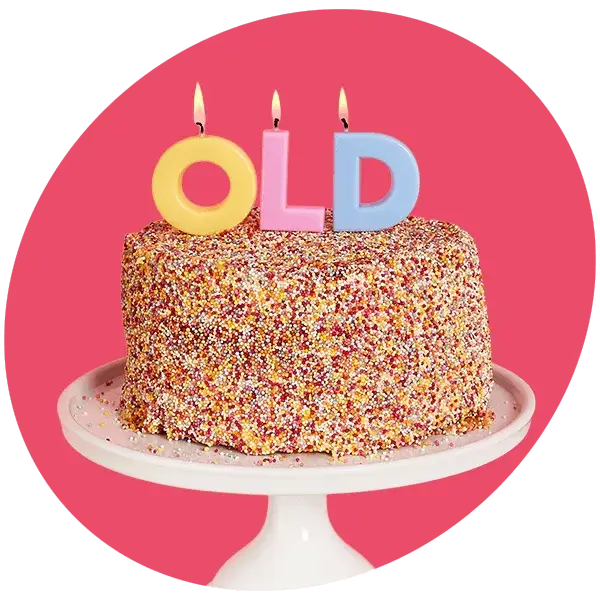 A sprinkle‑covered birthday cake topped with three lit candles shaped as the letters O, L, and D, displayed on a white cake stand against a bright pink background.