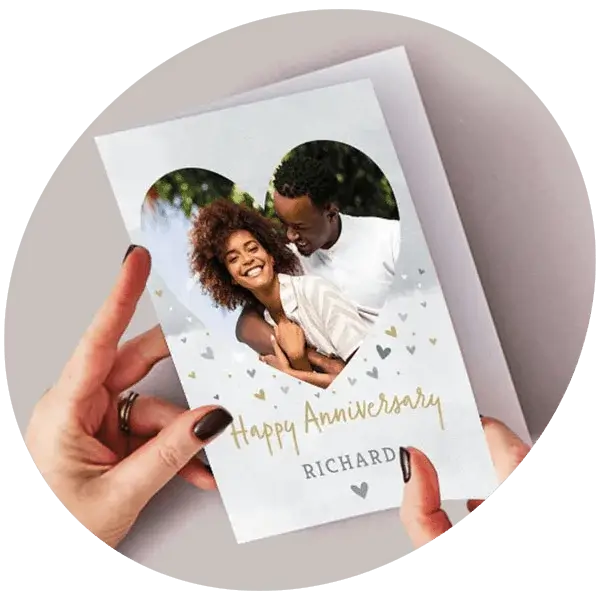A person holding an anniversary card featuring a heart‑shaped photo cutout and gold decorative text.