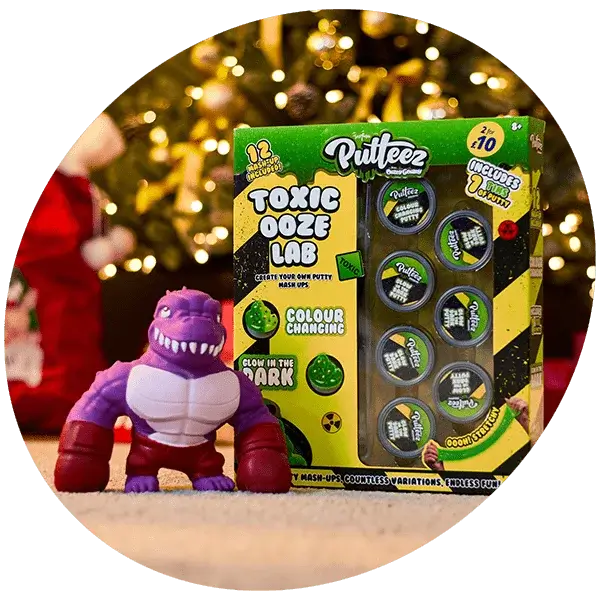 Toy set with a purple and white dinosaur figure and Putteez Toxic Ooze Lab kit containing 12 putty containers, displayed in front of a blurred Christmas tree.