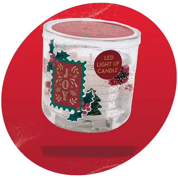 Clear glass LED light-up candle with festive decorations including holly leaves, berries, and the word JOY in gold lettering, displayed against a bright red background.