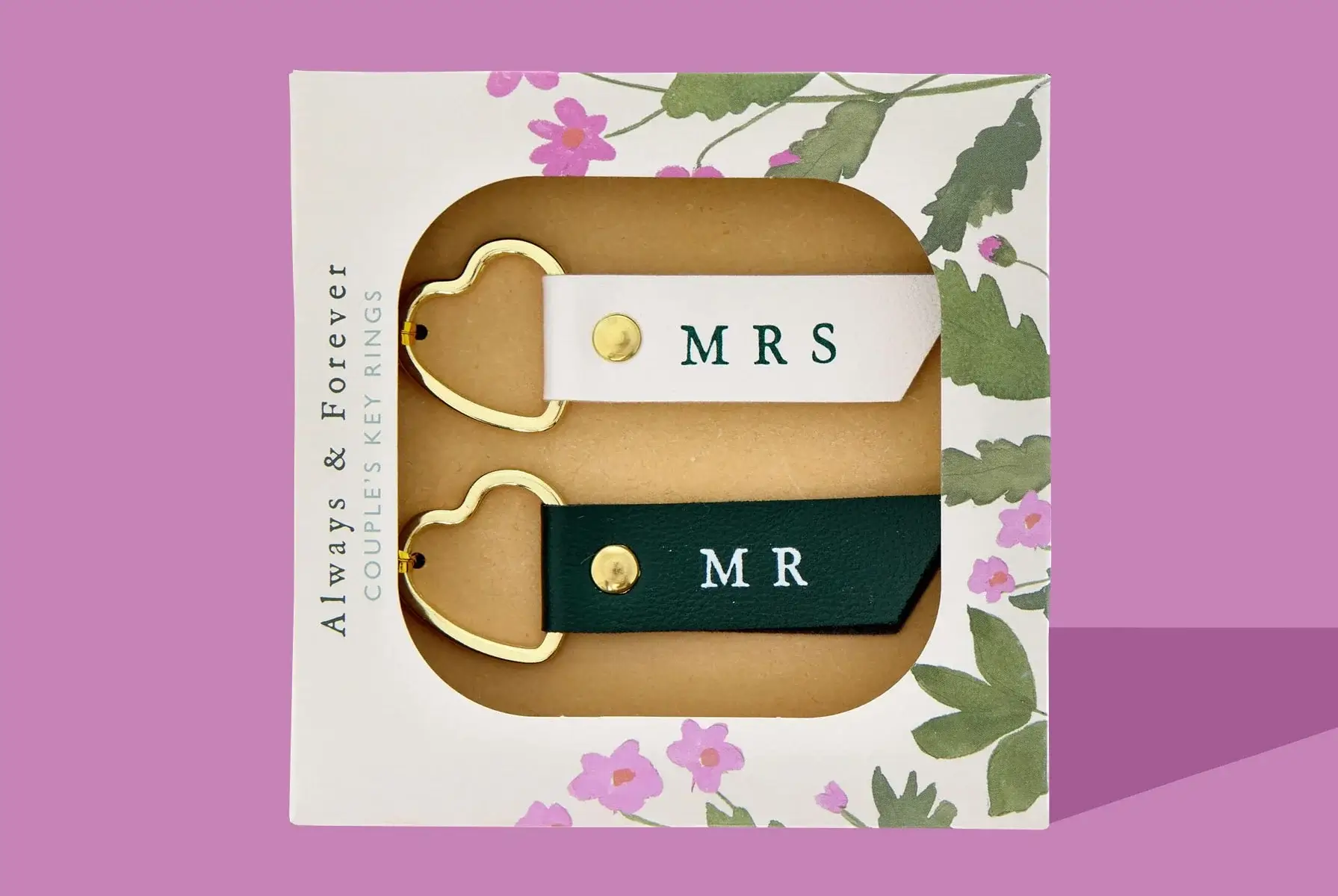'A pair of couple's keyrings in a floral-themed packaging. One keyring is white with the text 'MRS' and the other is black with the text 'MR'. Both keyrings have gold heart-shaped rings.' 'A pair of couple's keyrings in a floral-themed packaging. One keyring is white with the text 'MRS' and the other is black with the text 'MR'. Both keyrings have gold heart-shaped rings.'