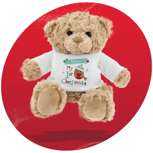 Brown teddy bear wearing a white sweater with colorful text that reads “My 1st Christmas” and a festive design, set against a bright red background.