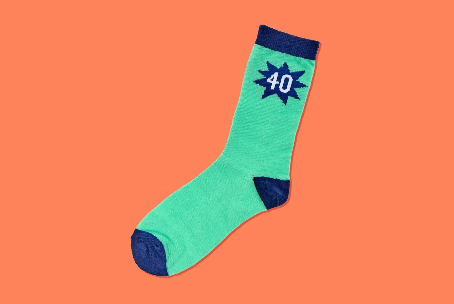 'A single green sock with dark blue accents on the toe, heel, and cuff. The sock has a dark blue starburst design near the top with the number 40 in white inside the starburst. The background is a solid orange color.' 'A single green sock with dark blue accents on the toe, heel, and cuff. The sock has a dark blue starburst design near the top with the number 40 in white inside the starburst. The background is a solid orange color.'