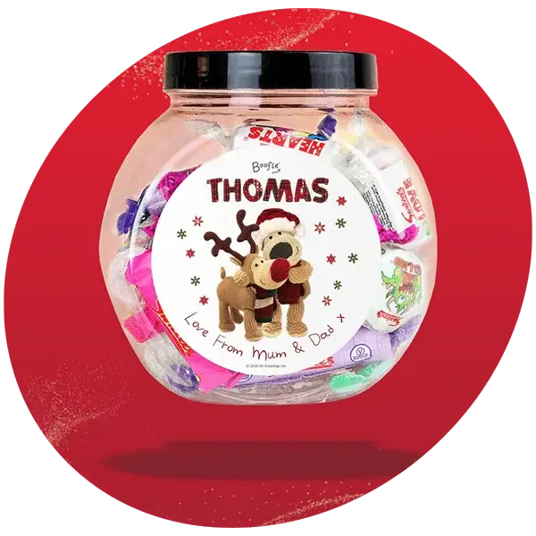 Clear jar filled with assorted colorful sweets, featuring a festive label with a reindeer illustration, the name Thomas, and the message Love From Mum & Dad, set against a red background with gold glitter accents.