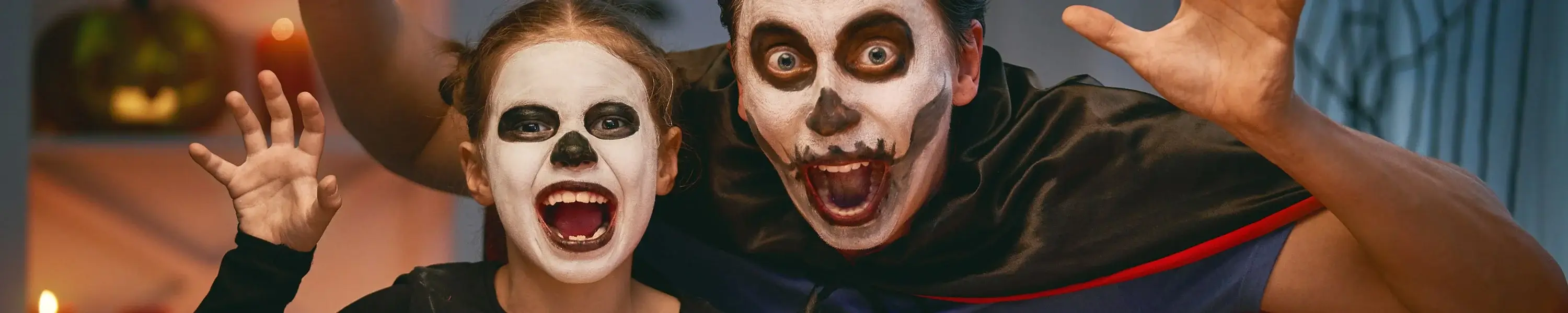 Two people in skull face paint and Halloween costumes pose with raised hands in a playful spooky gesture.