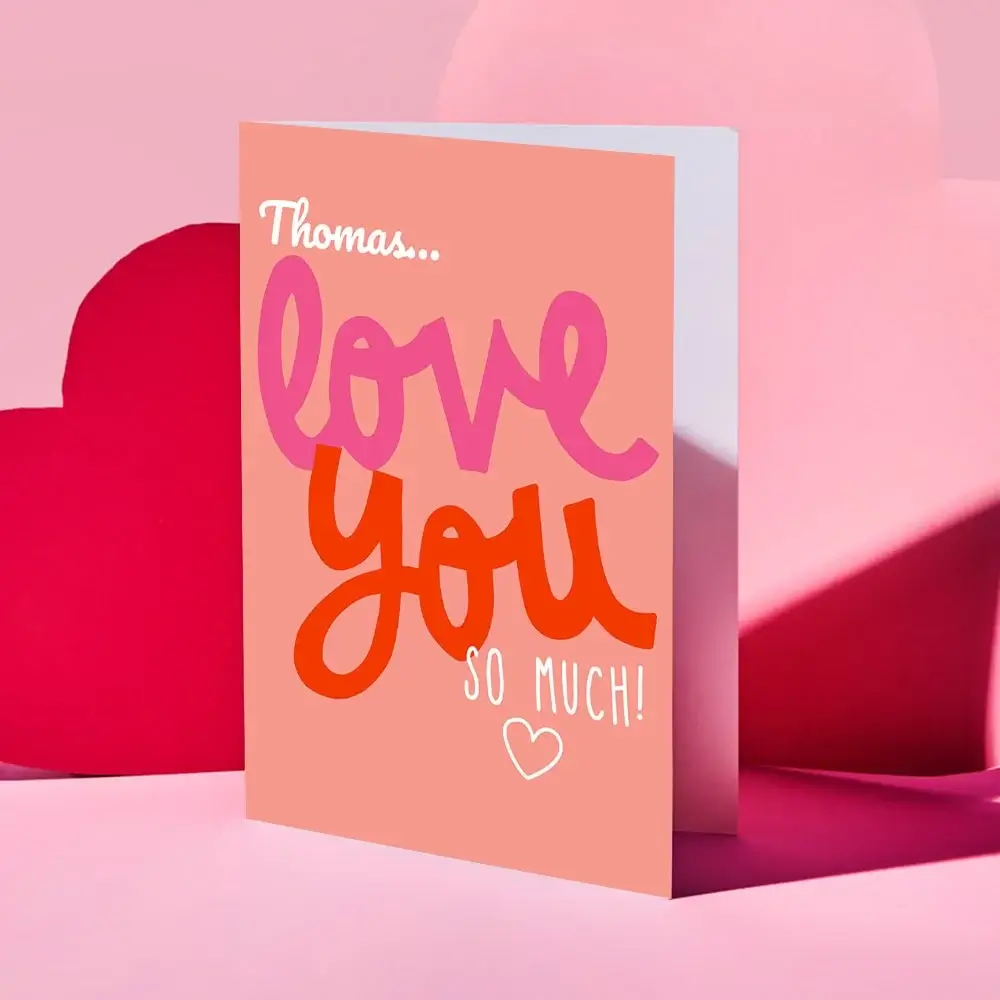 Black photo frame with a heart-shaped cutout at the top and three smaller rectangular photos below, featuring the text Bryan and Jen on a white background, set against a pink backdrop with heart shapes.