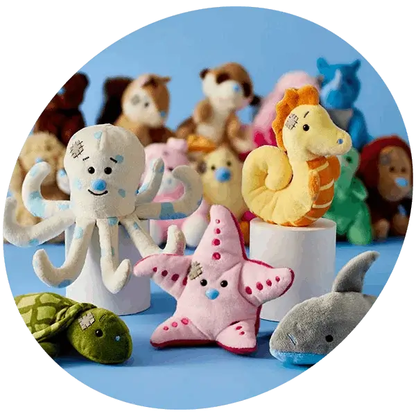 A collection of soft plush sea animal toys on a blue background, including an octopus, starfish, turtle, seahorse, and shark, arranged in a playful display.