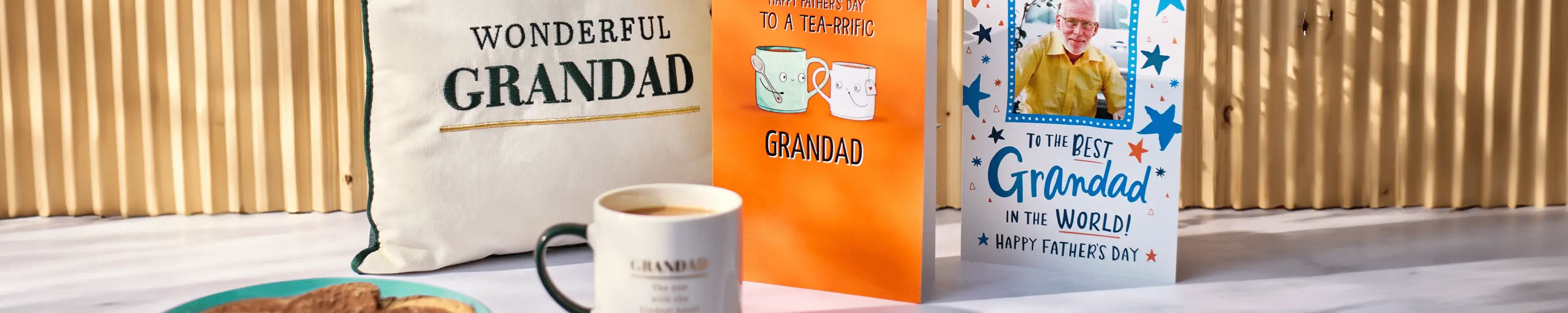 The image shows a collection of items arranged on a table, including a white tote bag with the text 'WONDERFUL GRANDAD', an orange greeting card with the text 'HAPPY BIRTHDAY TO A TERRIFIC GRANDAD' and images of two mugs, another greeting card with the text 'To the BEST Grandad in the WORLD! HAPPY FATHER'S DAY' and an image of a man holding a child, a plate of cookies, and a white mug with coffee. The image shows a collection of items arranged on a table, including a white tote bag with the text 'WONDERFUL GRANDAD', an orange greeting card with the text 'HAPPY BIRTHDAY TO A TERRIFIC GRANDAD' and images of two mugs, another greeting card with the text 'To the BEST Grandad in the WORLD! HAPPY FATHER'S DAY' and an image of a man holding a child, a plate of cookies, and a white mug with coffee.