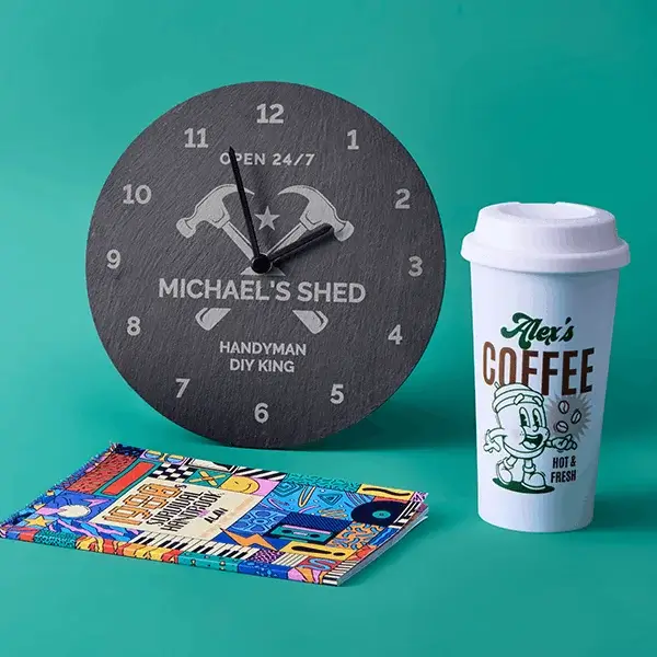 Personalised gift set featuring an engraved wall clock, reusable coffee cup, and colourful notebook on a teal background.
