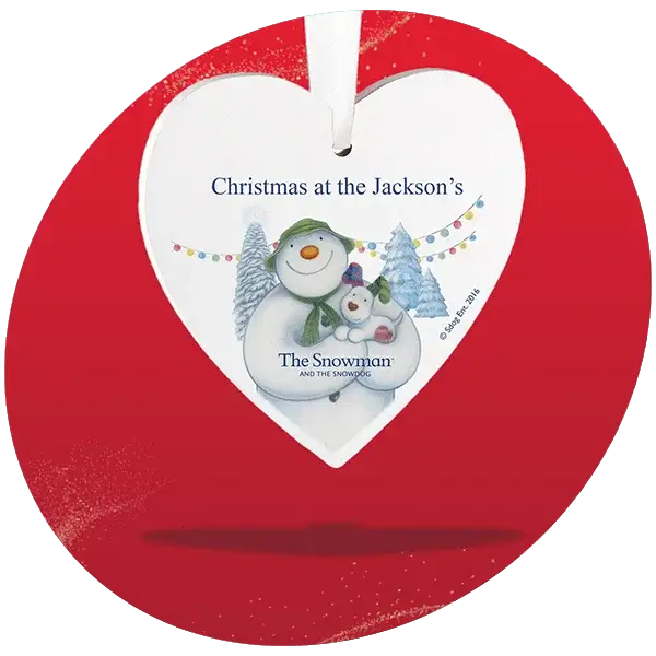 Heart-shaped Christmas ornament with snowman and snowdog illustration, snowy trees, colorful lights, and text Christmas at the Jackson's and The Snowman and The Snowdog. Heart-shaped Christmas ornament with snowman and snowdog illustration, snowy trees, colorful lights, and text Christmas at the Jackson's and The Snowman and The Snowdog.
