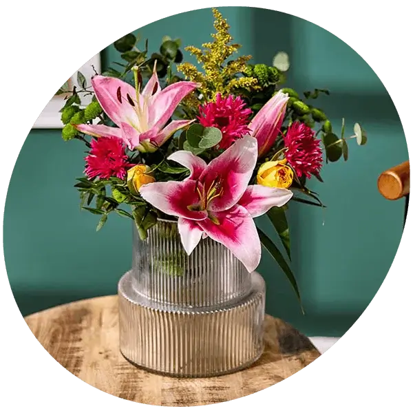 A bouquet of white and blue flowers with green foliage arranged in a tall ribbed white vase on a round table.