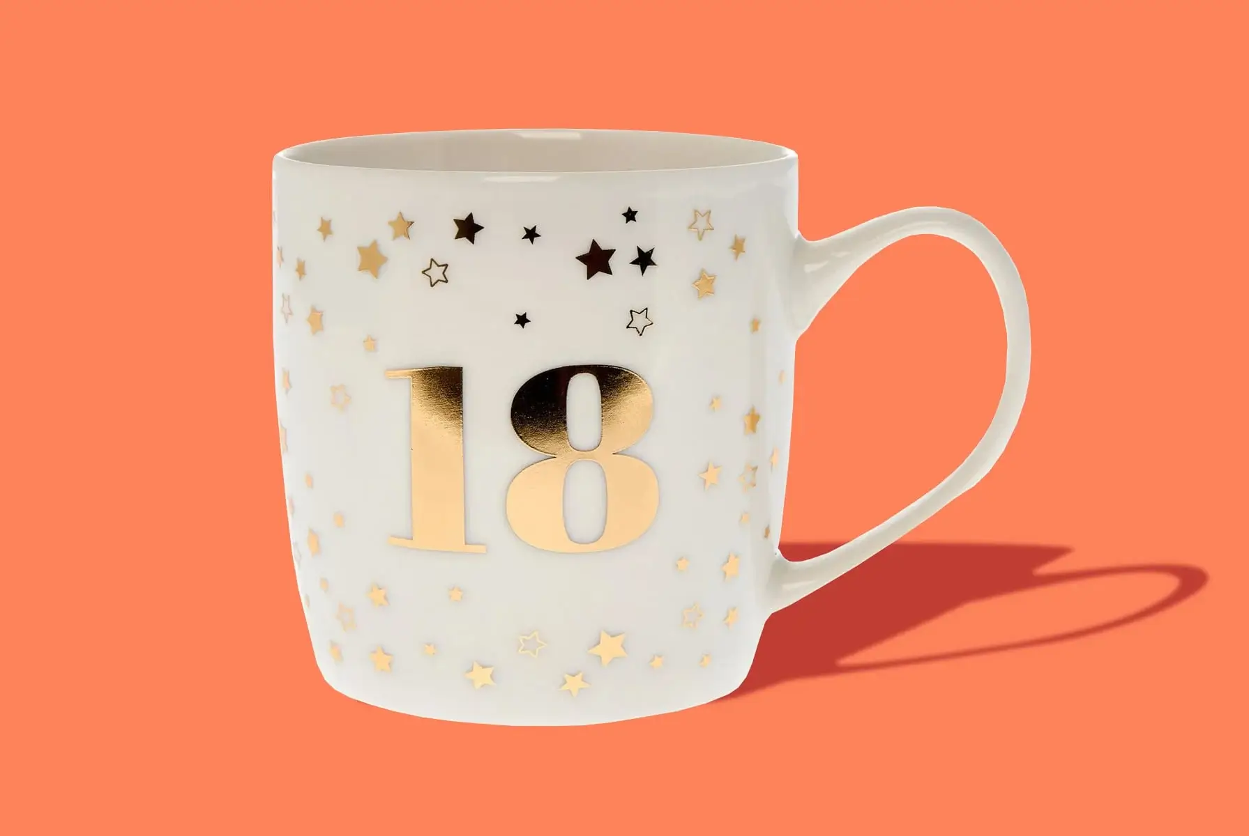 'A white ceramic mug with a large gold number 18 on it, surrounded by small gold and black stars, set against an orange background.' 'A white ceramic mug with a large gold number 18 on it, surrounded by small gold and black stars, set against an orange background.'