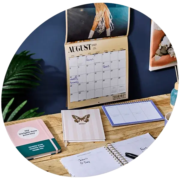 Personalised photo desk calendar with monthly planner layout displayed on a wooden desk alongside an open diary and pen.