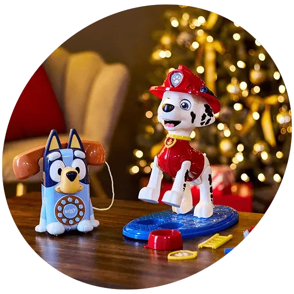 Toy Dalmatian dressed as a firefighter and blue dog-themed toy phone displayed in front of a decorated Christmas tree with lights.