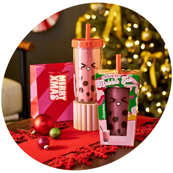 Strawberry bubble tea gift set with a pink cup and straw, festive packaging, and Christmas decorations in front of a lit tree.